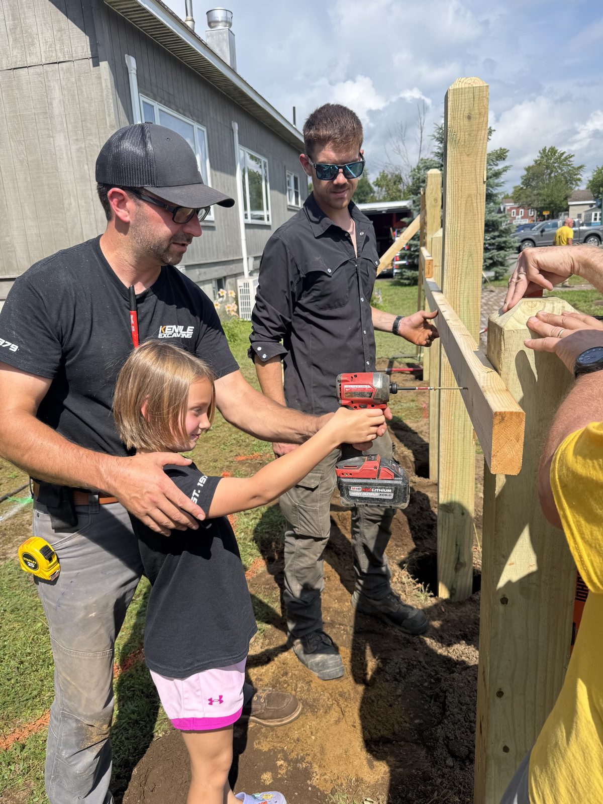 A father guiding his young daughter as she drives a screw into a fence post