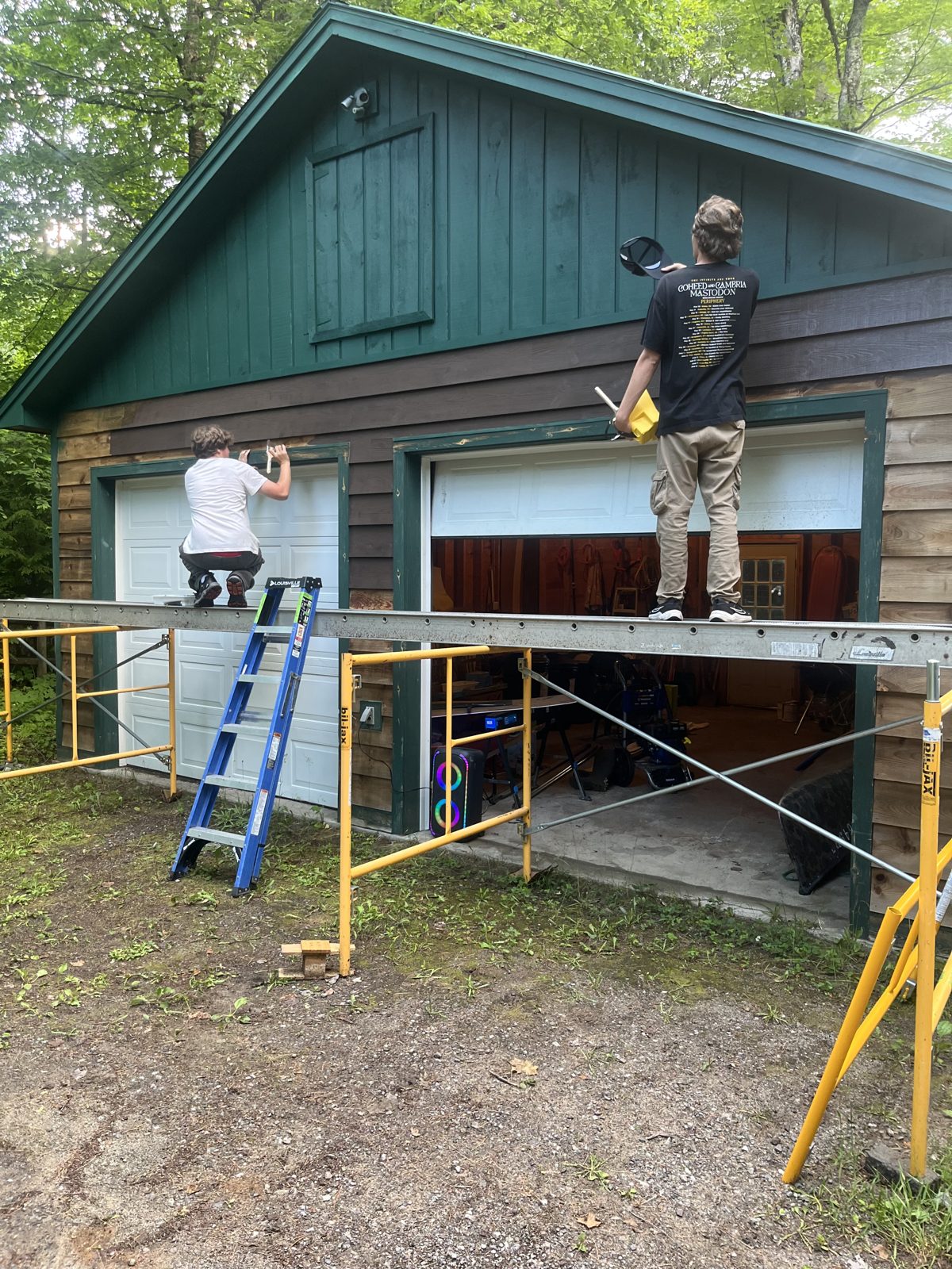 Two Tupper Lake students painting a garage from scaffolding